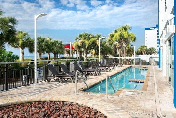 A pool area with lounge chairs, palm trees, and a building in the background.