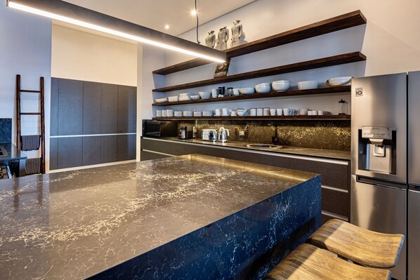 A modern kitchen with a marble countertop, built-in shelves, and a stainless steel refrigerator.