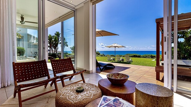 Un balcón espacioso con vistas al océano, muebles de madera y un ventanal que da al interior.