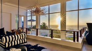 Un salón amplio con un gran ventanal con vista al océano, una lámpara colgante y un sofá a rayas.