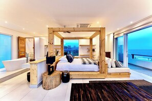 Ein modernes Schlafzimmer mit einem großen Bett, einem Holzkopfende und Blick auf den Ozean.
