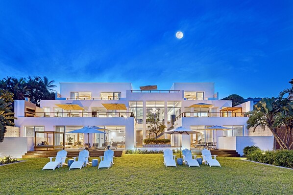 Ein modernes, zweistöckiges Haus mit gepflegtem Rasen, einer Sitzgelegenheit im Freien und einem großen Mond am Himmel.