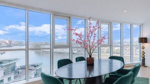 Een eetgedeelte met een ronde tafel, groene stoelen en een vaas met roze bloemen.