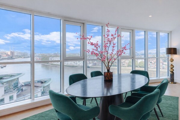 A dining area with a round table, green chairs, and a vase with pink flowers.