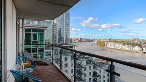 Een balkon met uitzicht op een rivier, moderne gebouwen en een glazen hekwerk.