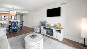 Una sala de estar moderna con comedor, un televisor de pantalla plana en la pared y un mueble blanco para entretenimiento con objetos decorativos.