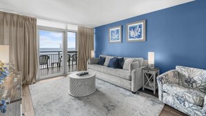 Un salón con pared azul, sofá gris, una mesita de centro redonda y un sillón estampado.