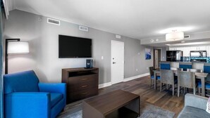 Un salon moderne avec un téléviseur à écran plat, un canapé bleu, une table basse en bois et un coin repas avec des chaises bleues.