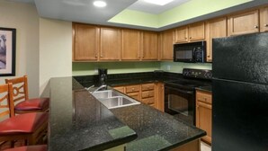 A kitchen with wooden cabinets, a black refrigerator, a microwave, and a sink. - Tropical Tranquility: 1BR Condo with Ocean Access (Myrtle Beach)