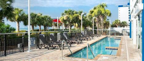A pool area with lounge chairs, palm trees, and a building in the background.