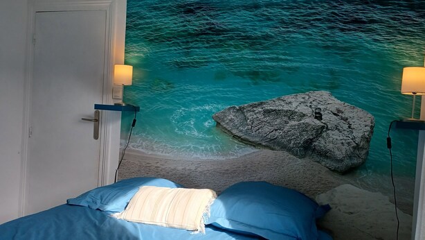 A bedroom with a bed, a nightstand, and a wall mural of a beach scene. - Appartement 3 Pièces Avec Terrasse au Calme Hyper Centre Arcachon - Mer à 50 m (Arcachon)
