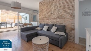 A modern living room with a grey sectional sofa, a round coffee table, and a brick accent wall. - Appartement 3 Pièces Avec Terrasse au Calme Hyper Centre Arcachon - Mer à 50 m (Arcachon)