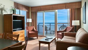 Une chambre d’hôtel avec un balcon, une télévision, une table à manger et deux canapés.