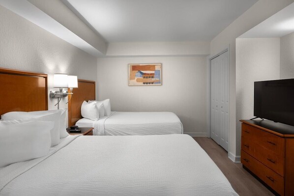A hotel room with two beds, a TV, a dresser, and a painting on the wall.