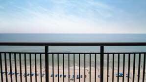 A beach view from a balcony with a railing, ocean, and beach umbrellas. - Seascape Sanctuary: Oceanfront Escape with 4 Beds (Myrtle Beach)