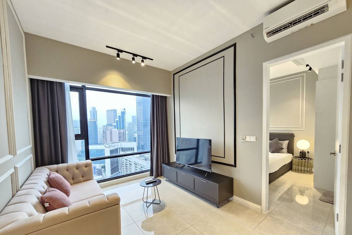A modern hotel room with a sofa, TV, and a city view.