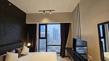 A modern hotel room with a large bed, a flat-screen TV, and a city view through large windows.