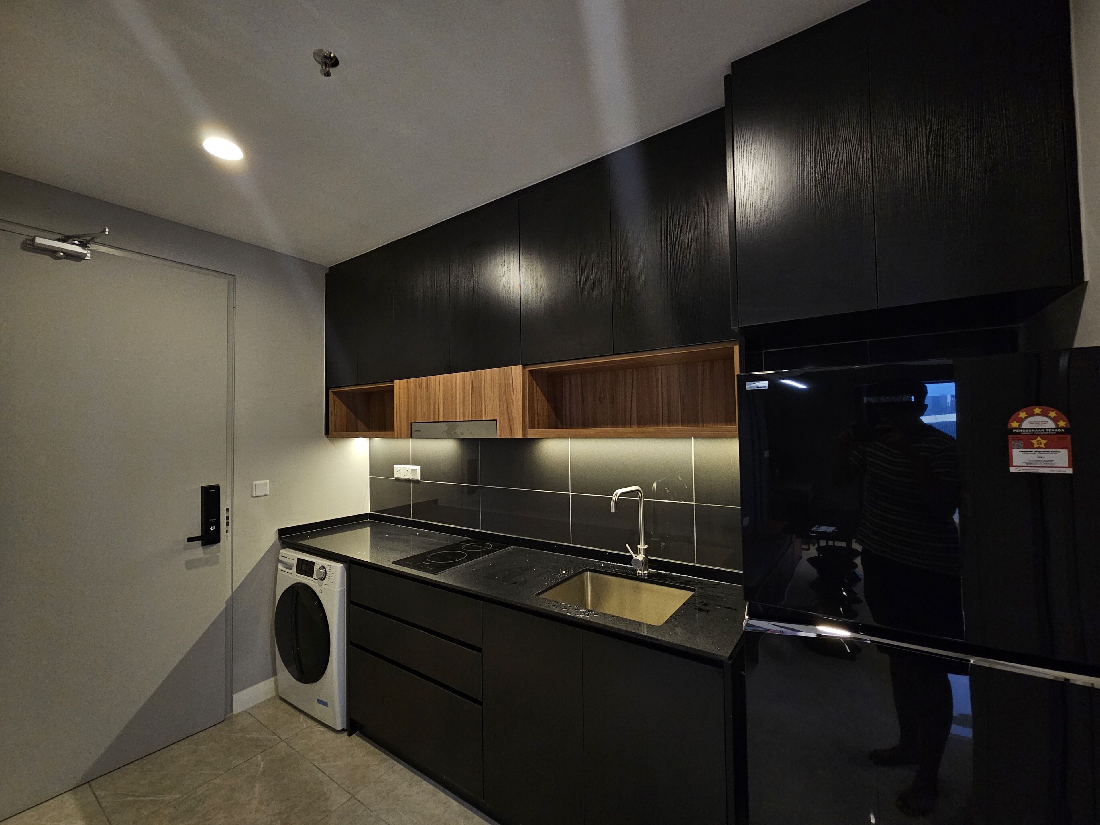 Una cocina moderna con armarios negros, un lavamanos de acero inoxidable y una lavadora integrada.