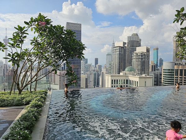 Une piscine à débordement offrant une vue sur les gratte-ciel de la ville, entourée de verdure et de bâtiments modernes.