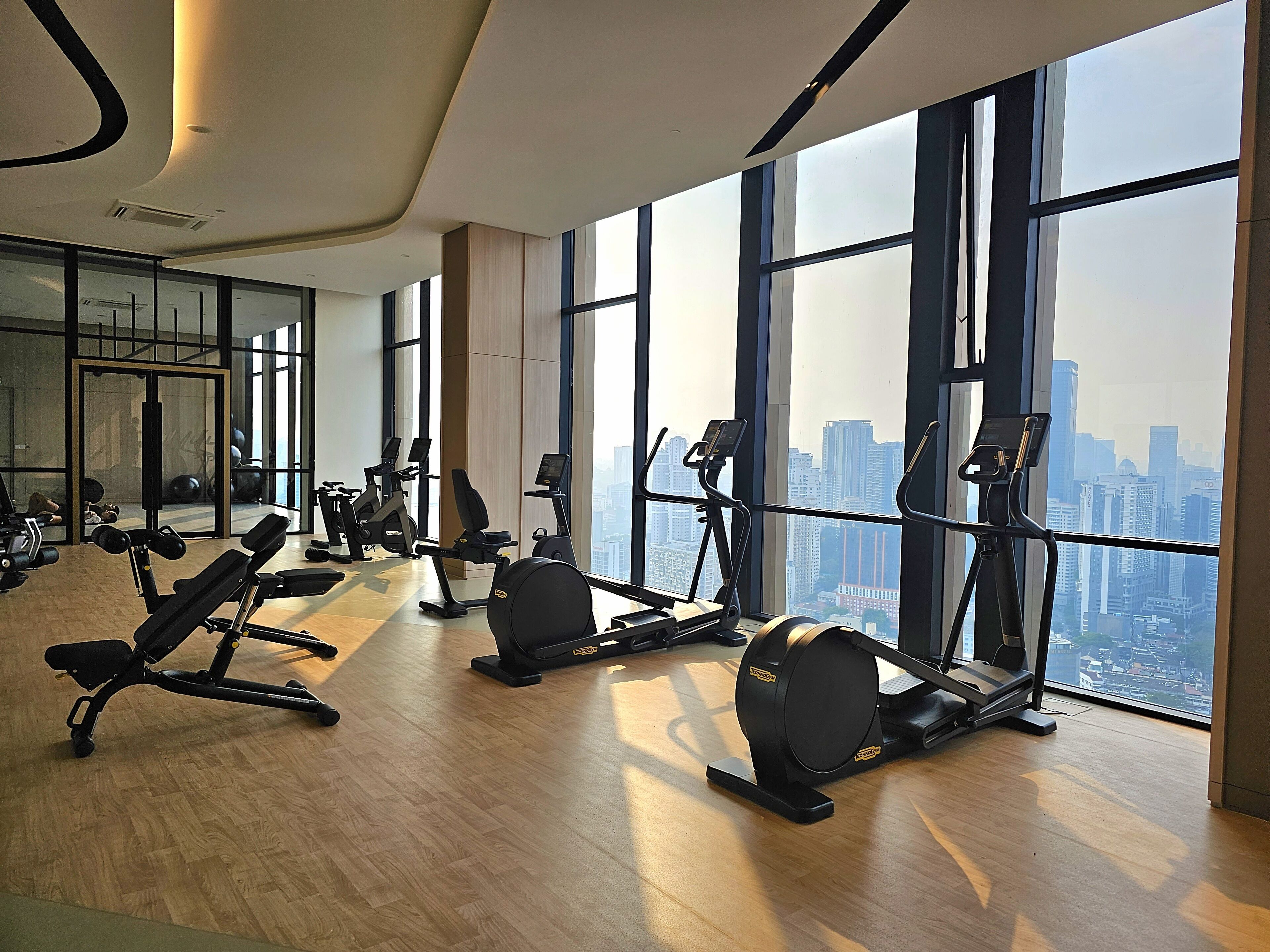 A gym with various exercise equipment, large windows, and a city view.