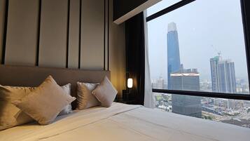 A modern hotel room with a large bed, a view of a cityscape through a large window, and a city skyline visible outside.