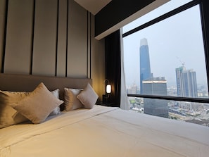Une chambre d’hôtel moderne avec un grand lit, une vue sur le paysage urbain à travers une grande fenêtre et une vue dégagée sur les bâtiments de la ville.