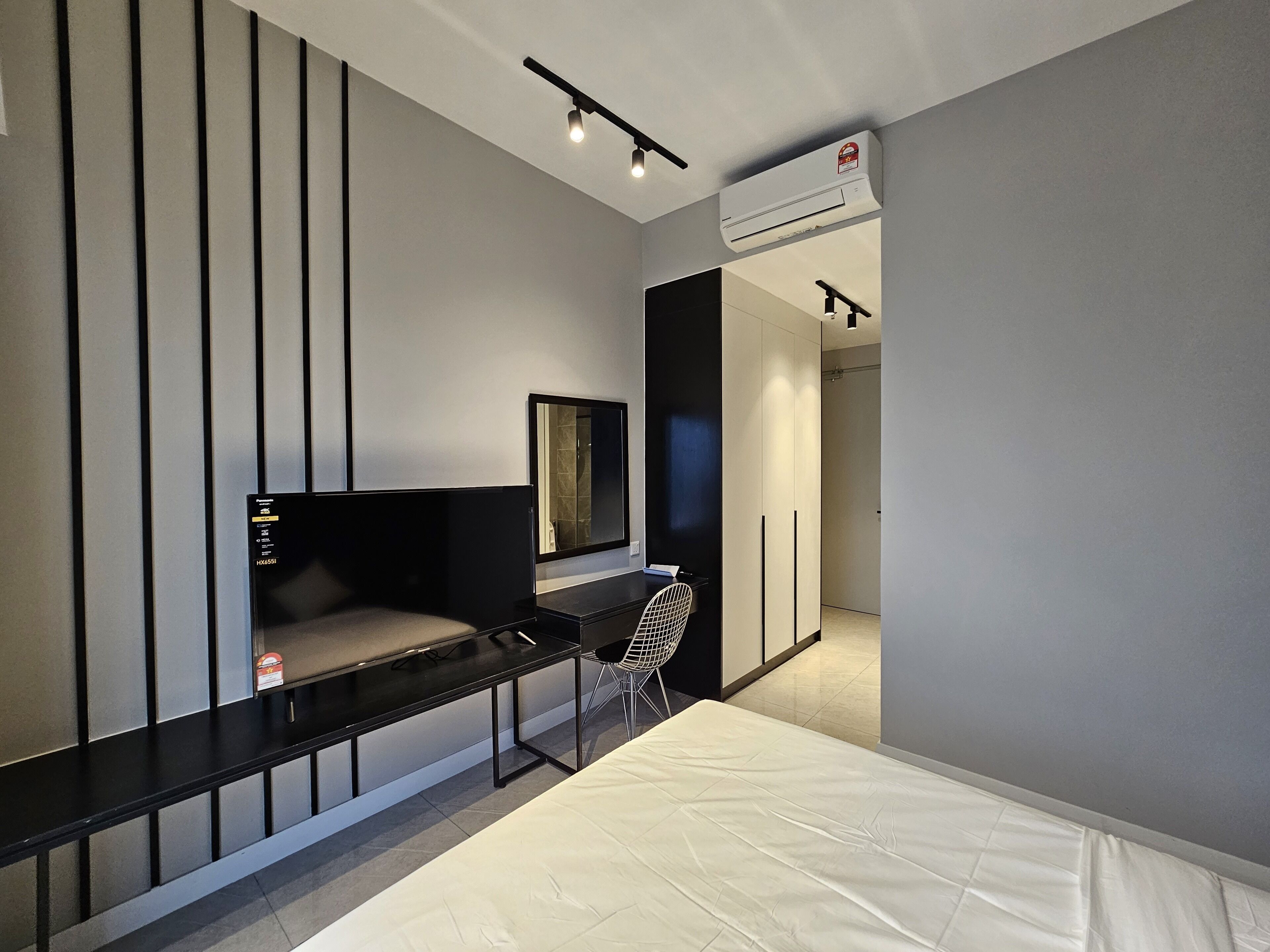 A modern hotel room with a bed, a desk with a chair, a TV, and an air conditioning unit.