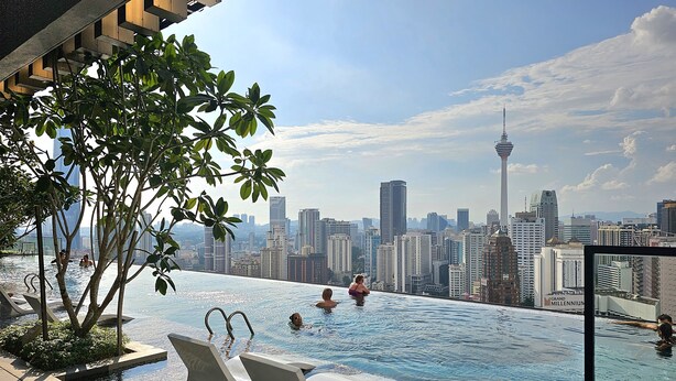 An infinity pool with city views, lounge chairs, and a modern architectural setting.