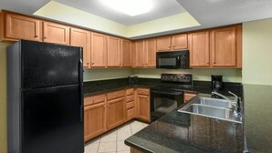 A kitchen with wooden cabinets, a black refrigerator, a microwave, an oven, and a sink.