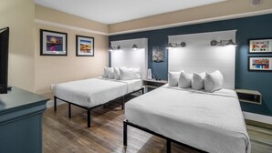 A hotel room with two beds, a TV, framed pictures on the wall, and a blue accent wall.