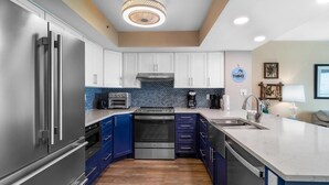 A modern kitchen with stainless steel appliances, blue cabinets, and a white countertop.
