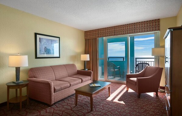 A hotel room with a sofa, armchair, coffee table, and a large window with a view of the ocean. - Waveside Getaway 2BR Stunning Ocean Views (Myrtle Beach)