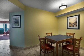 A dining area with a table and four chairs, framed pictures on the walls, and a ceiling light fixture. - Waveside Getaway 2BR Stunning Ocean Views (Myrtle Beach)