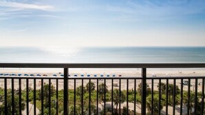Ein Balkon mit Blick auf einen Strand, Palmen und einen klaren Himmel.