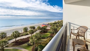 A balcony with a view of a beach, palm trees, and a red structure. - Beachfront Harmony 2BR Dual Ocean Balconies (Myrtle Beach)