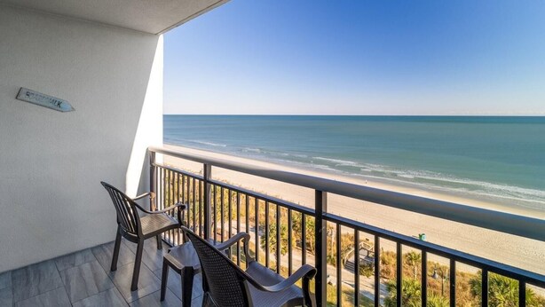A balcony with a view of the ocean, a sign indicating a boardwalk, and two chairs. - Oceanfront Tranquility: 2BR Retreat Dual Balconies (Myrtle Beach)