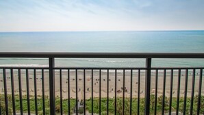 Vista sulla spiaggia da un balcone con ringhiera, cielo sereno e mare calmo.