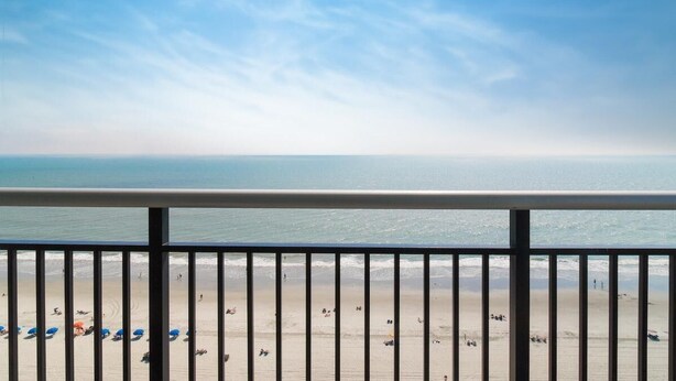 A beach view from a balcony with a railing, sandy beach, and ocean. - Beach Lover's Haven with Ocean-View Balconies (Myrtle Beach)