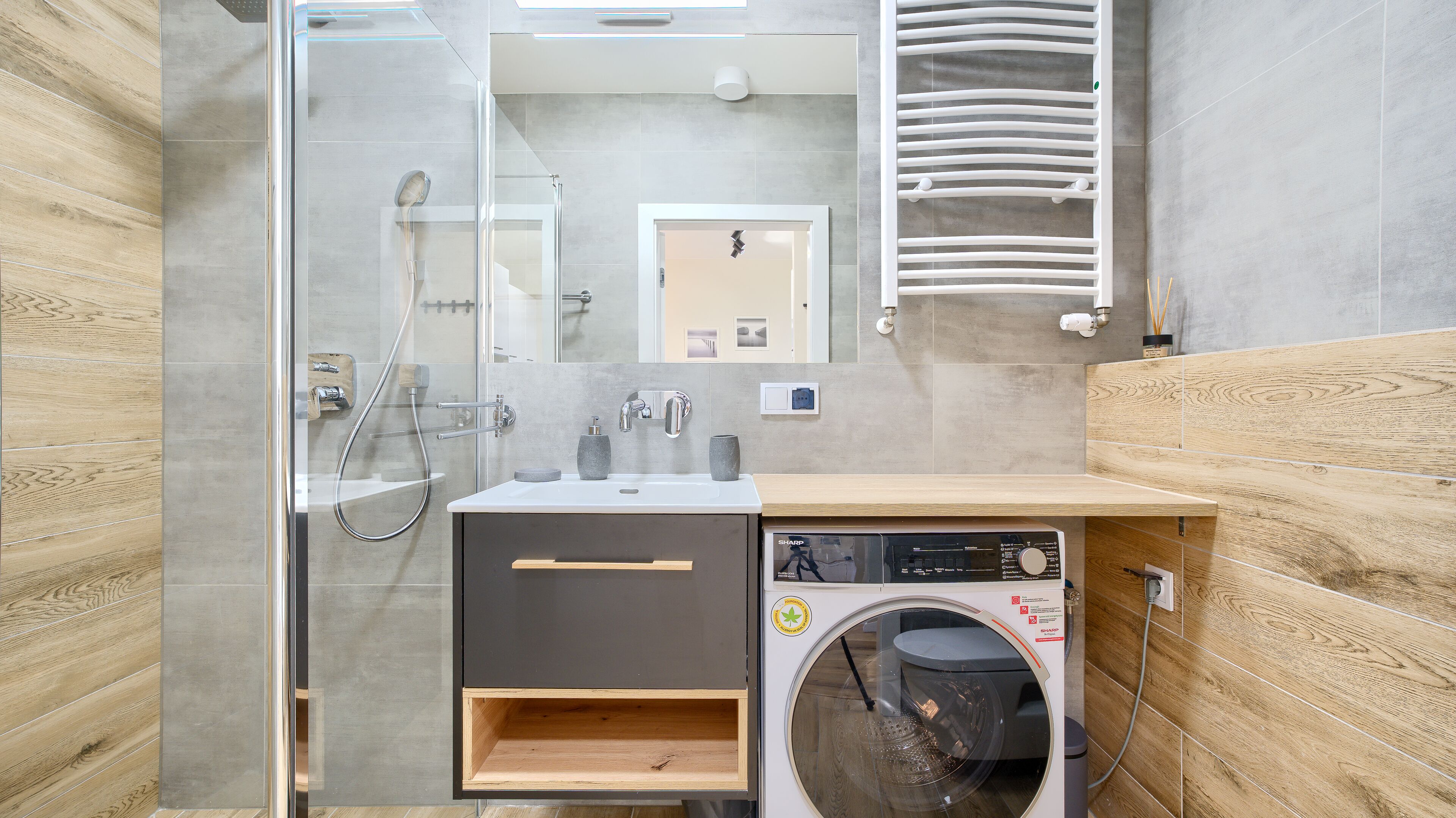 Une salle de bain moderne dotée d’une douche à parois de verre, d’un lave-linge encastré et d’un meuble-lavabo en bois.