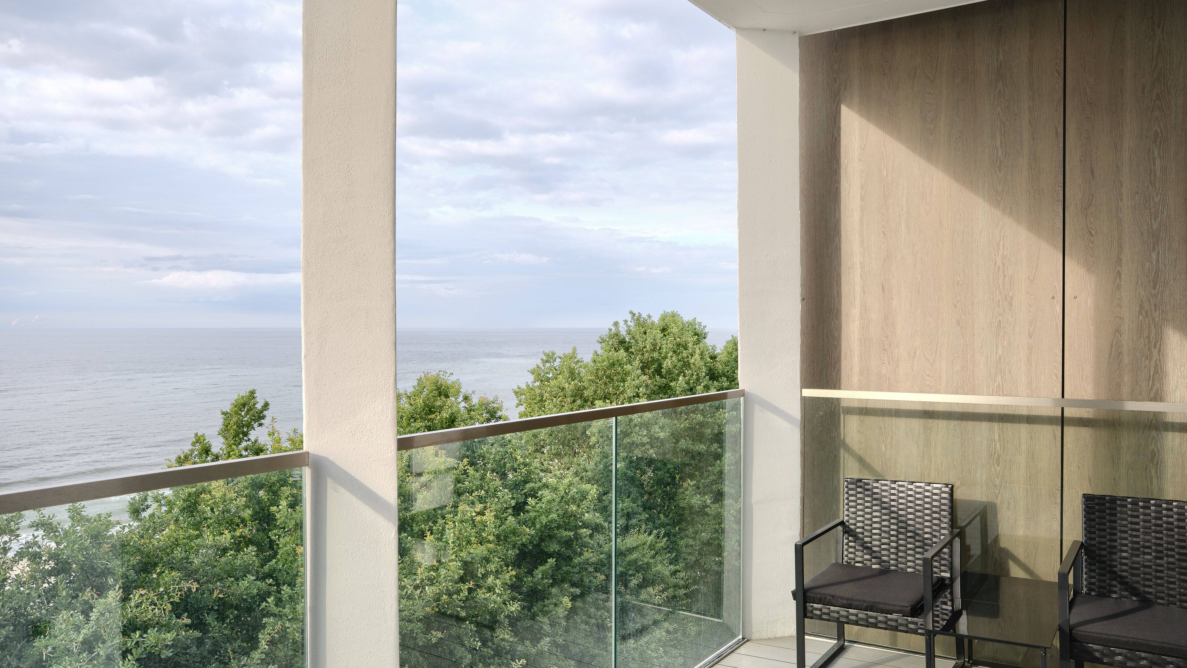 A balcony with a view of the sea, two chairs, and a wooden wall.
