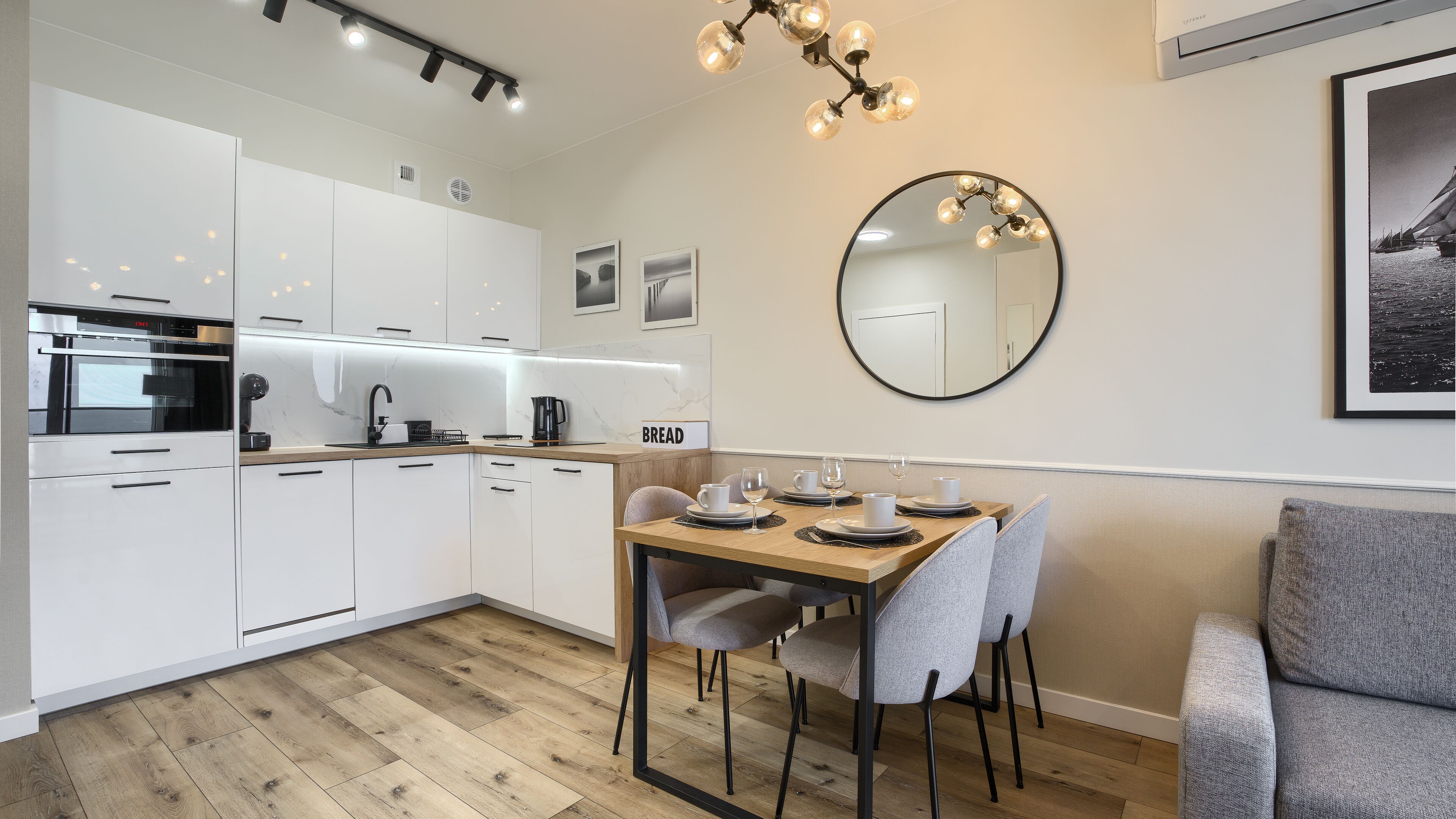 Een moderne keuken met witte kastjes, een houten eettafel met borden en glazen, en een ronde spiegel aan de muur.