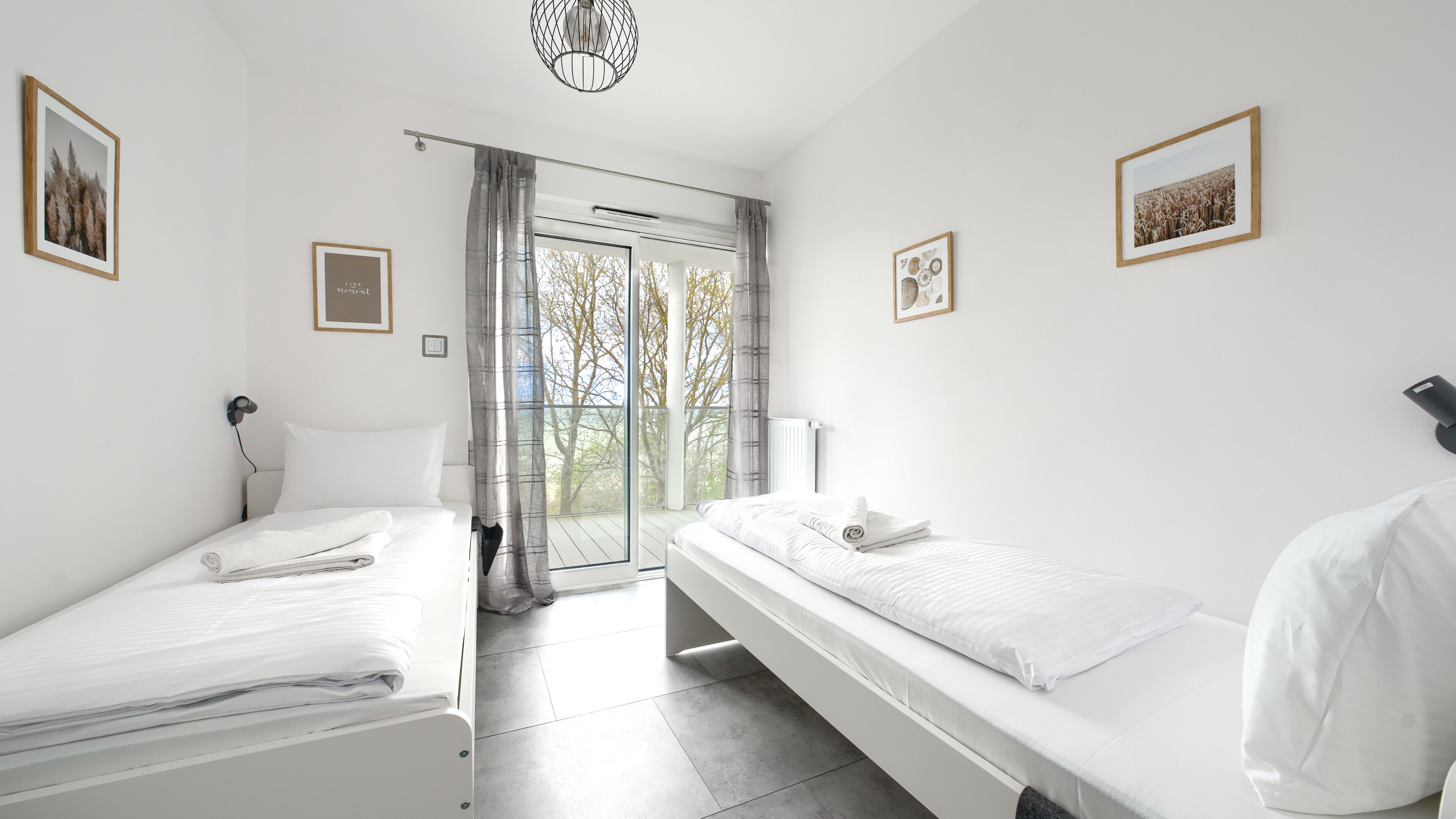 Une chambre moderne avec deux lits, une grande fenêtre donnant sur la forêt et des tableaux encadrés accrochés aux murs.