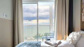 Habitación de hotel con cama, vista al mar y balcón con una silla y una mesa.
