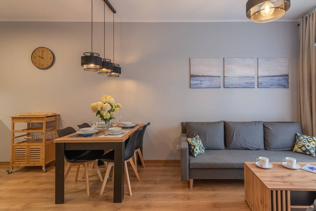 Ein modernes Wohnzimmer mit Essbereich, einer Sofagarnitur, einem Holztisch und einer Wanduhr.