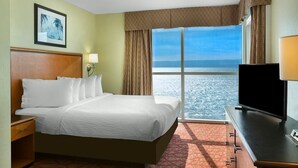Ein Hotelzimmer mit Bett, Fernseher, Schreibtisch und einem Fenster mit Meerblick.