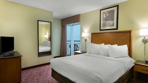 A hotel room with a large bed, a television on a wooden cabinet, a mirror, a window with curtains, and a framed picture on the wall. - Penthouse Elegance on the Boardwalk 4 Bdrm 4 Bath (Myrtle Beach)