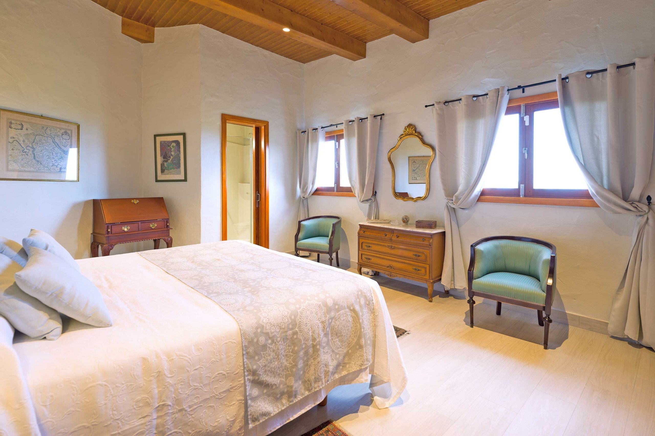 A bedroom with a bed, two chairs, a dresser, and a mirror.