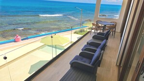 Een balkon met uitzicht op de oceaan, een tafel en stoelen, en een gele parasol.