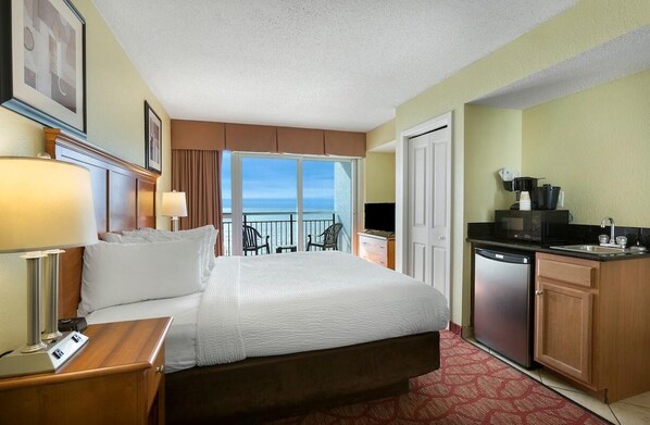 Une chambre d’hôtel comprenant un lit, des lampes de chevet, un petit bureau, un coin cuisine avec un réfrigérateur et un balcon avec vue.