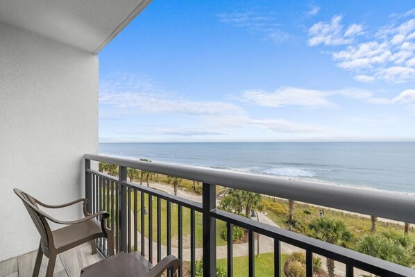 A balcony with a view of the ocean, a chair, and a table.